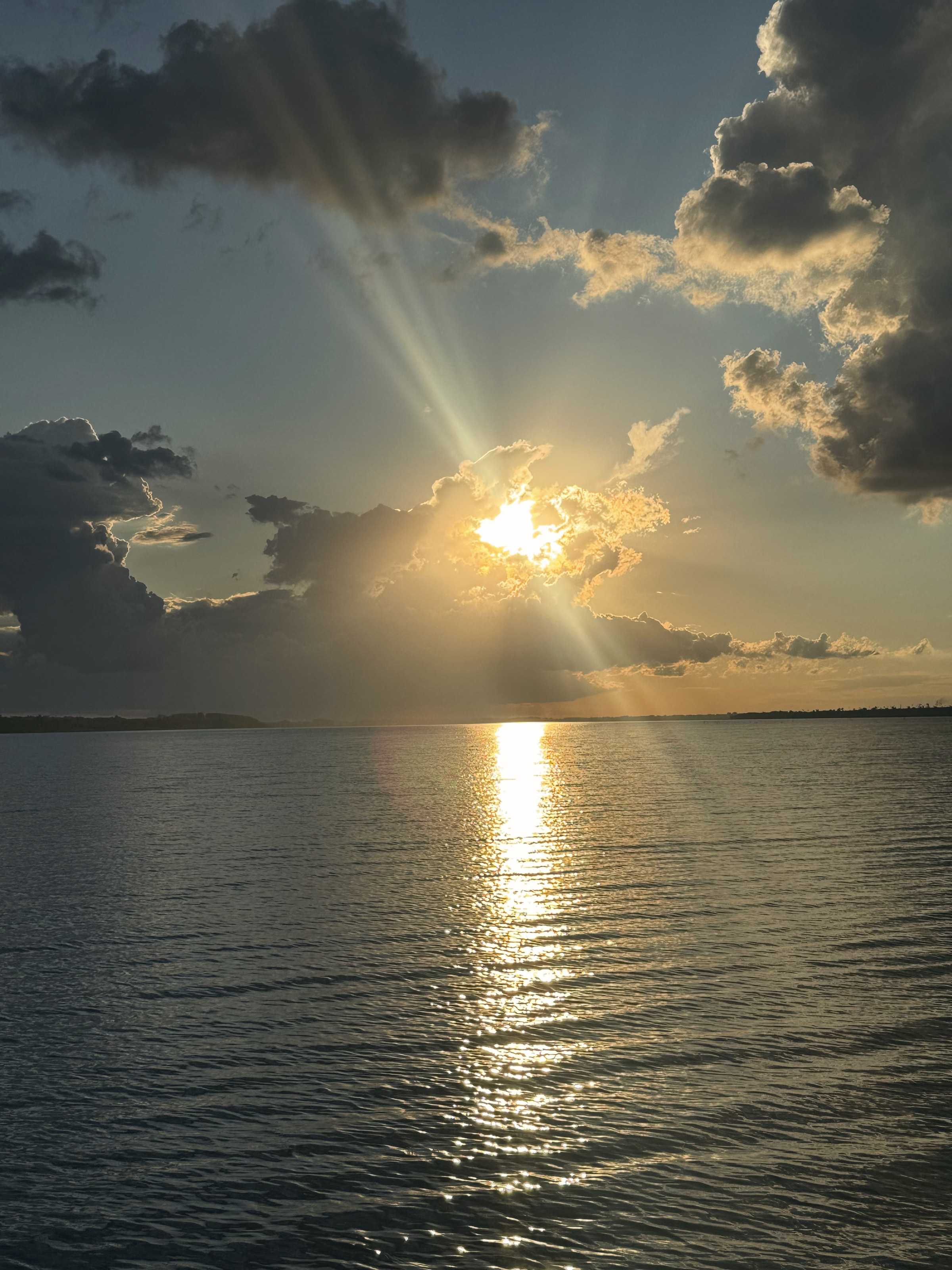 El sol se pone entre nubes sobre el lago y deja un reflejo dorado en el agua.