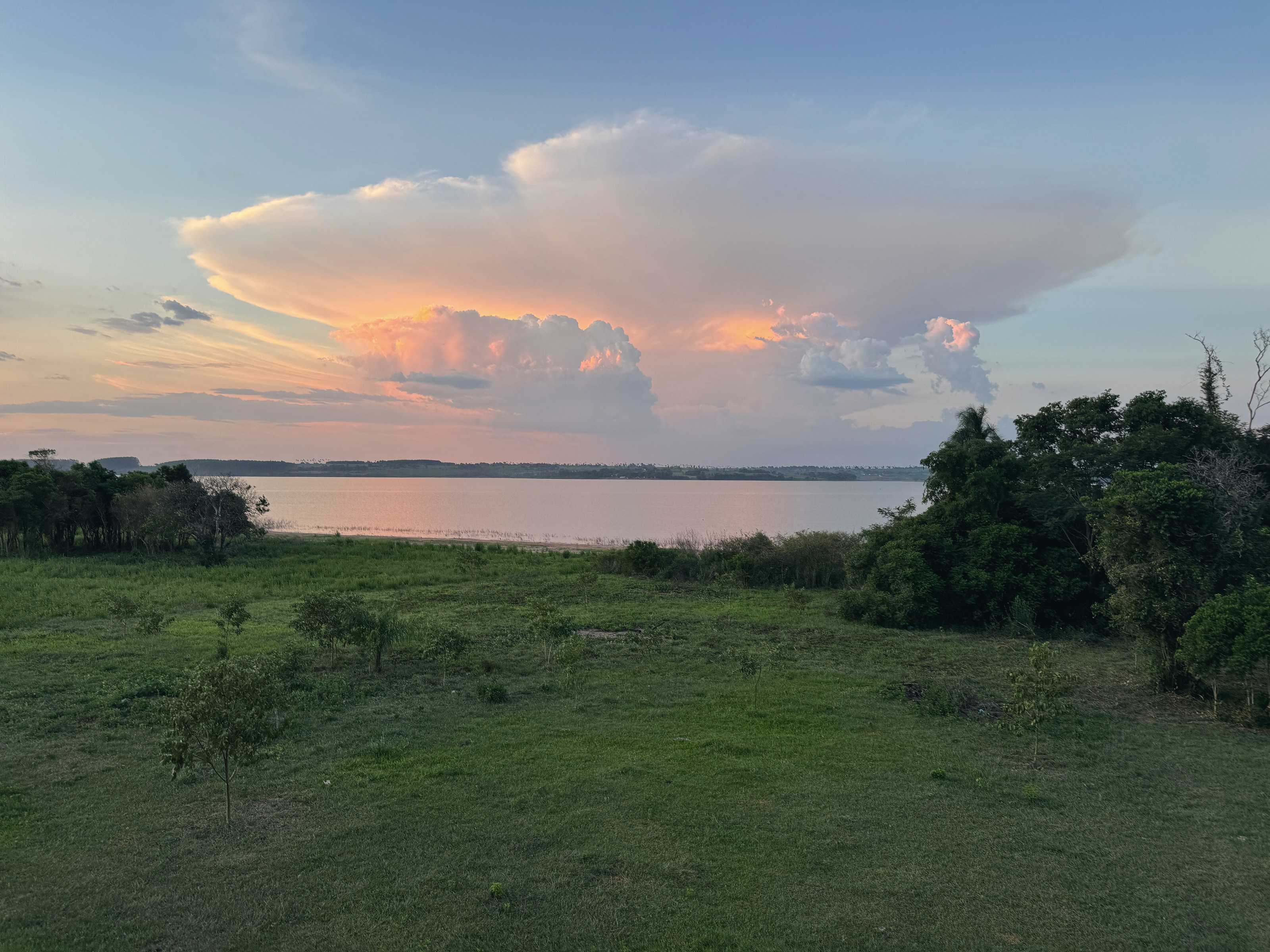 Un cúmulo enorme, rosado por el atardecer, sobre el lago quieto y el campo.