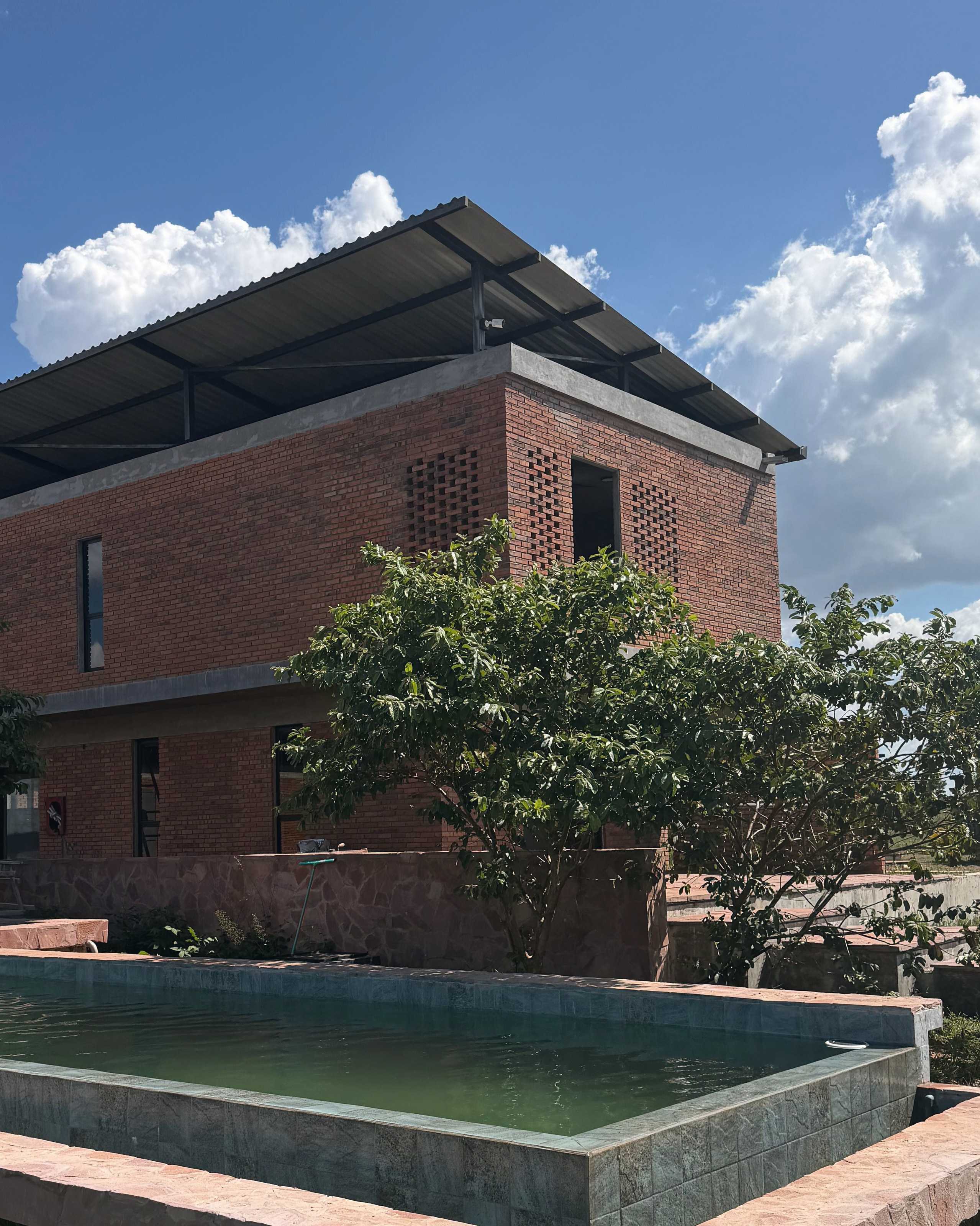 El edificio de ladrillo visto con muros de celosía, junto a la piscina de agua verde y borde de piedra rosada.